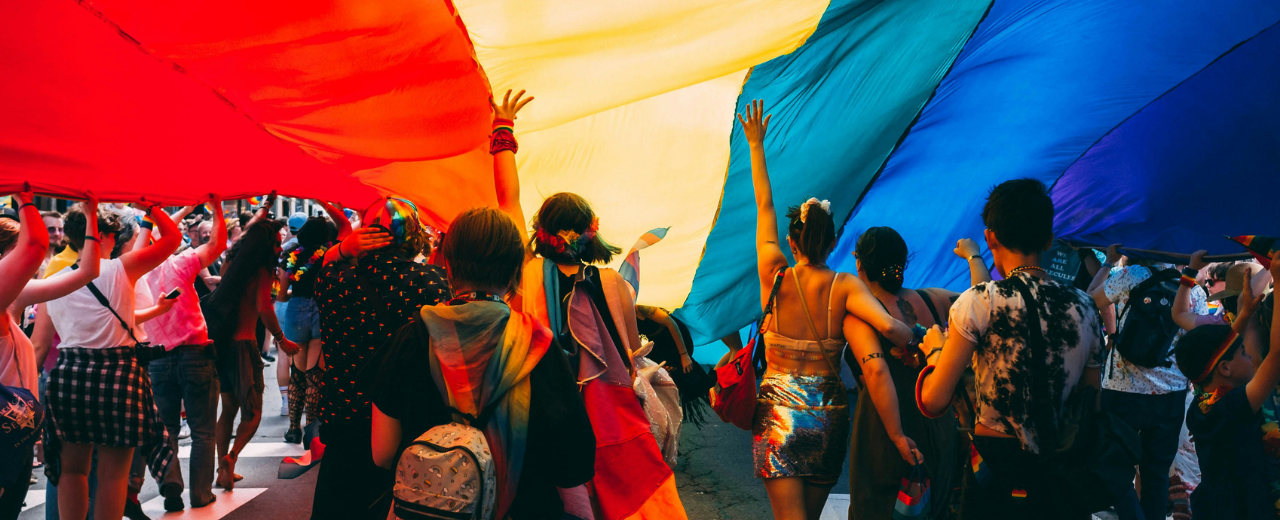 Menschen unter einer Pride Flagge laufen